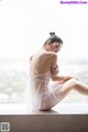 A woman in a white lingerie sitting on a window sill.