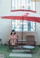 A woman sitting on a bench under an umbrella.