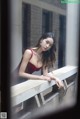 A woman in a red dress leaning against a window.