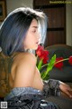 A woman with blue hair sitting on a couch holding a red flower.