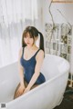 A woman in a blue bathing suit sitting in a bathtub.