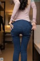 A woman in a pink shirt and blue jeans is standing in front of a mirror.