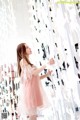 A woman in a pink dress standing in front of a wall of paper cranes.