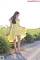 A woman in a yellow dress standing on a dirt road.