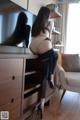 A woman sitting on top of a dresser in front of a television.