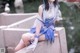 A woman in a blue and white dress sitting on a ledge.