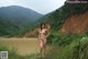 A naked woman standing next to a body of water.