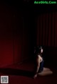 A woman sitting on the floor in front of a red curtain.