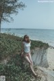 A woman in a white tank top sitting on a rock by the ocean.