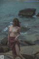 A naked woman standing on a rock by the ocean.