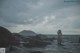 A naked woman standing in the water near rocks.