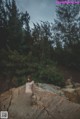 A naked woman sitting on a rock in the woods.