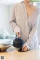 A woman pouring tea into a black teapot on a table.