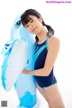 A woman in a blue and white swimsuit holding an inflatable whale.