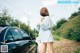 A woman standing next to a black car on a dirt road.