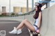 A woman sitting on a skateboard on the side of a road.